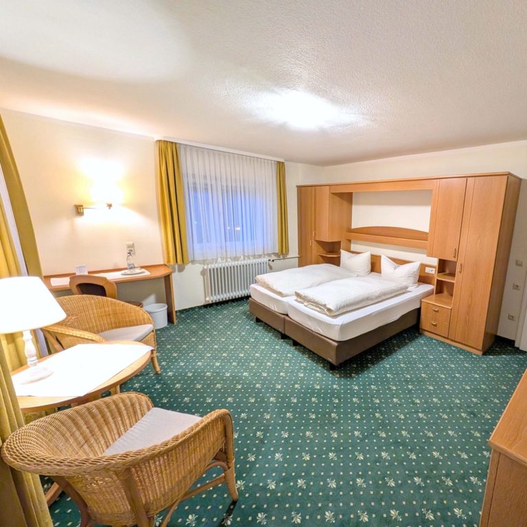 Zimmer Hotel Fidelitas Helles Hotelzimmer mit zwei Betten, Sitzbereichen und Stühlen.